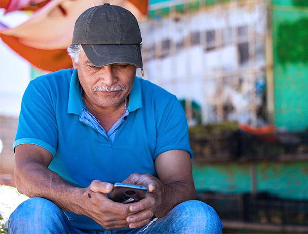 Man wearing a hat and blue polo, sitting outside of a store looking at his smartphone